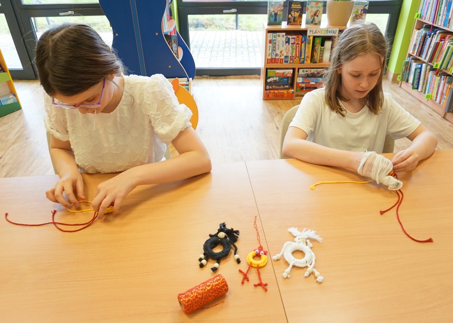 dwie uczestniczki zajęć podczas pracy na zajęciach zaplatają czerwone i żółte sznurki, jedna z dziewczynek ma na dłoni bandaż