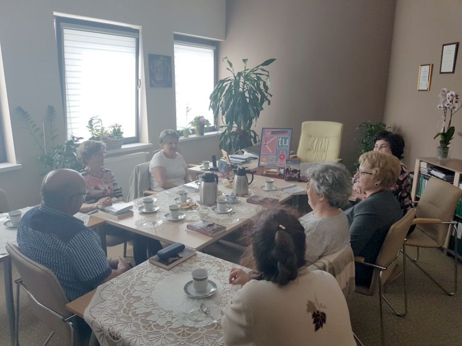 7 OSÓB ZEBRANYCH PRZY STOŁACH ROZMAWIA MIĘDZY SOBĄ