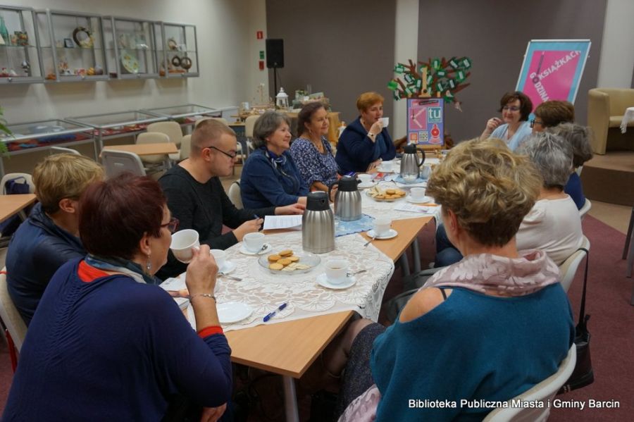 Zebrani uczestnicy spotkania siedzą przy stolikach i rozmawiają o przeczytanej książce.