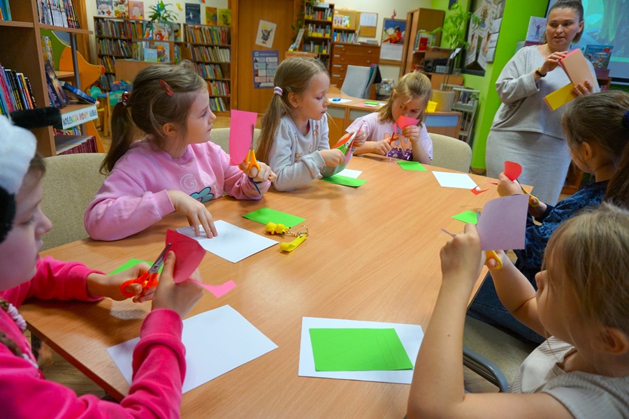 Grupa dzieci przy stole, przed nimi leżą białe i zielone kartki, oraz nożyczki