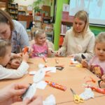 bibliotekarka pomaga jednej z dziewczynek biorących udział w zajęciach skleić pracę