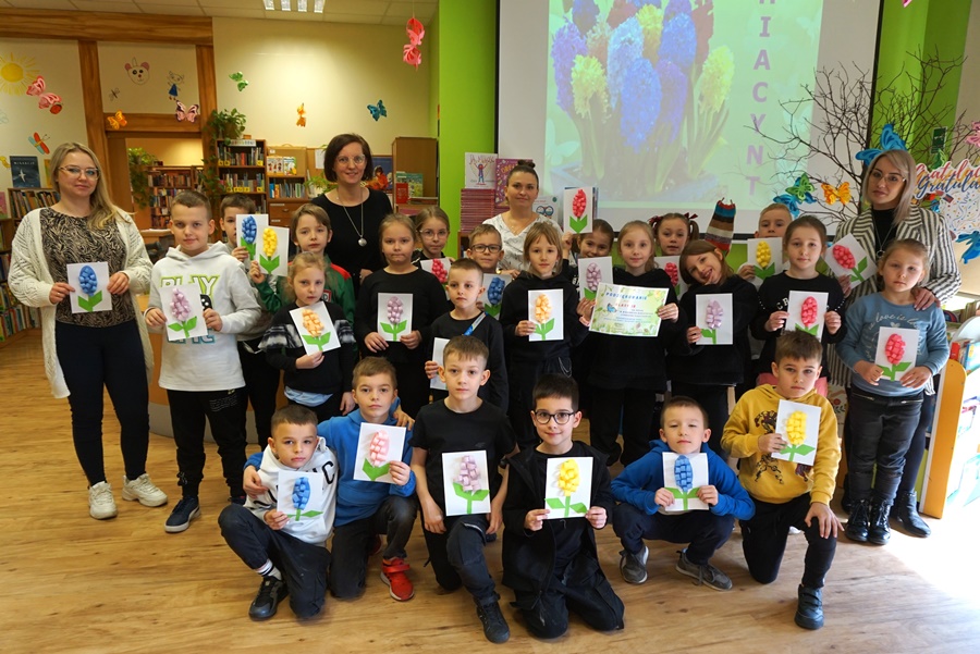 grupowe zdjęcie bibliotekarek, uczniów i nauczycieli klasy biorącej udział w zajęciach, dzieci trzymają wykonanie prace