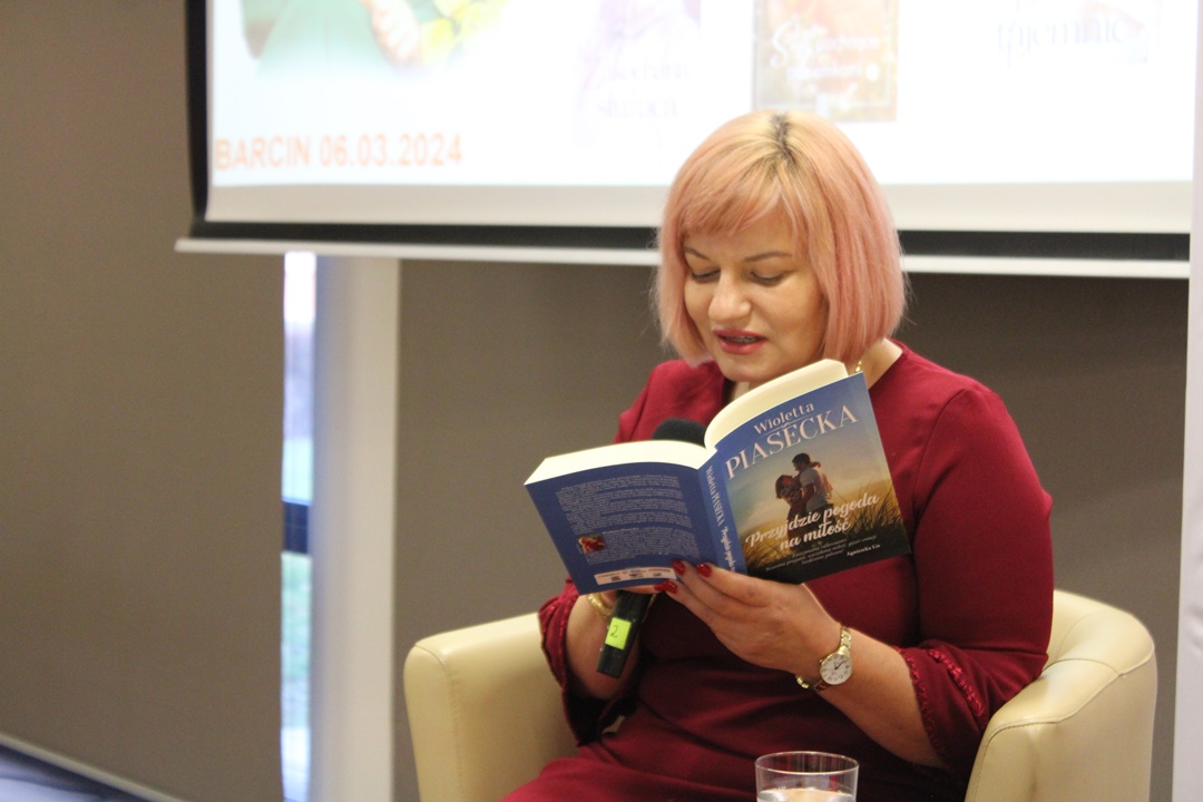 Wioletta Piasecka, siedząc w beżowym fotelu czyta fragment książki pt. "Przyjdzie pogoda na miłość"