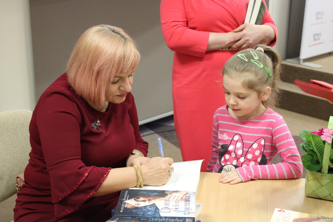 Wioletta Piasecka podpisuje książkę przyniesioną przez małą dziewczynkę.