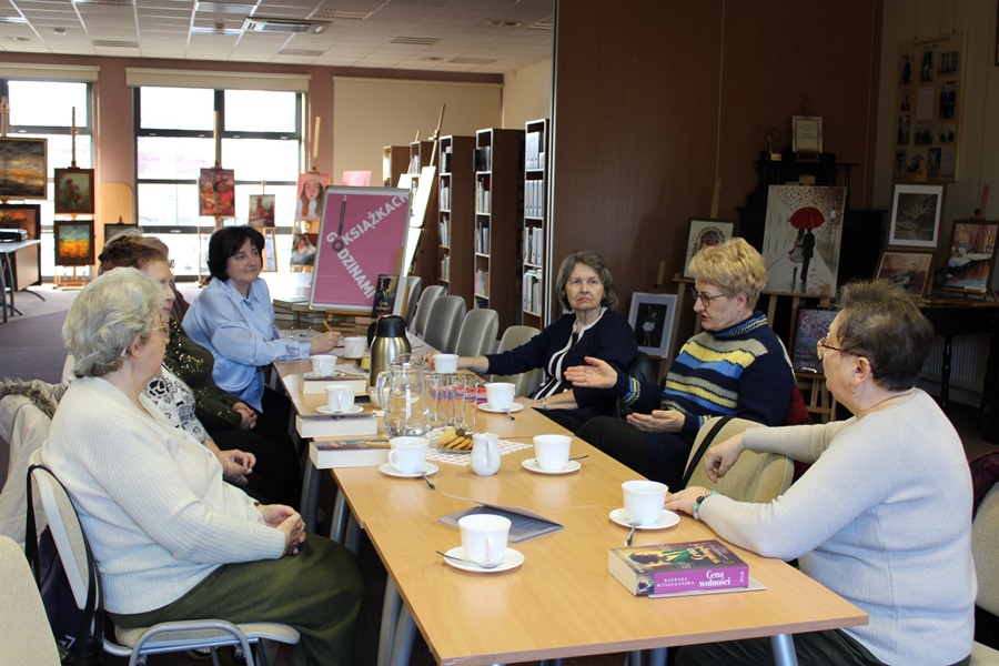 7 uczestniczek spotkania siedzi wzdłuż stołów i dyskutuje na temat omawianej książki