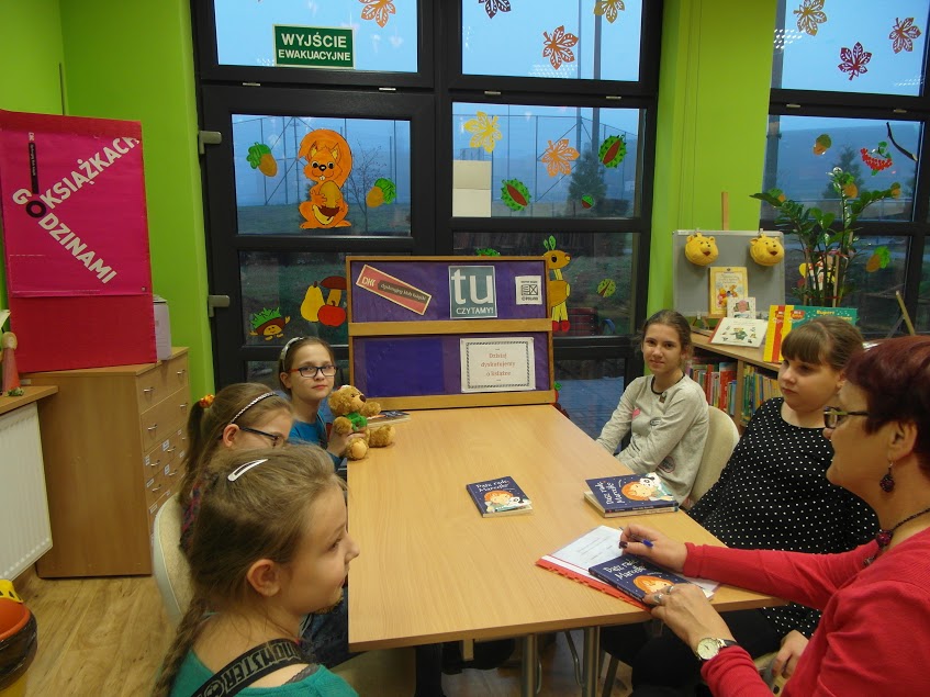 5 dziewczynek razem z bibliotekarką prowadzącą spotkanie siedzą wokół stołu, na stole leżą omawiane książki.