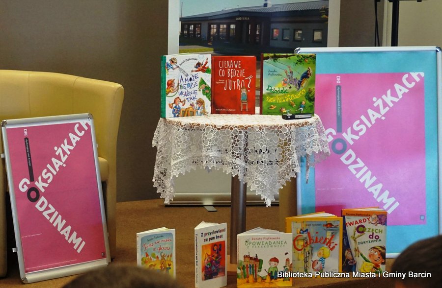 Książki ustawione na okrągłym stoliku jak również pod nim, po bokach stolika stoją plakaty z napisem "Godzinami o książkach"