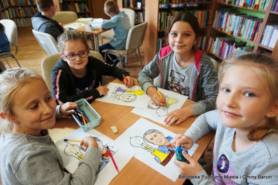 4 dzieci siedzi przy stole i koloruje wybrane przez siebie obrazki, wszyscy patrzą w stronę obiektywu aparatu.