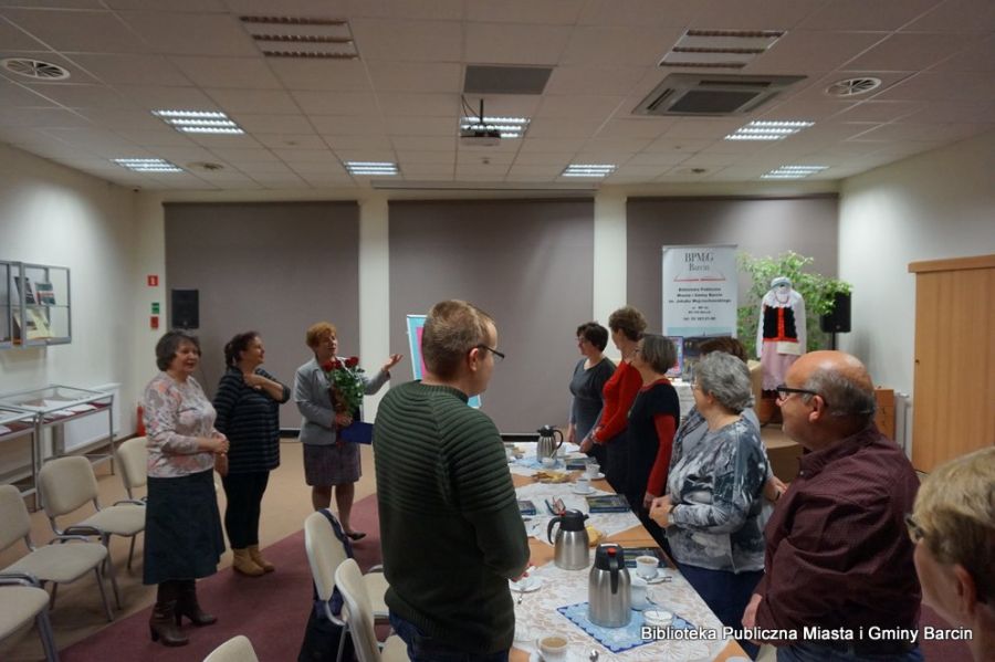 Grupa 11 stojących osób, dyrektor biblioteki Grażyna Szafraniak trzyma w rękach bukiet róż.