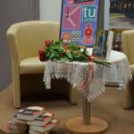 Okrągły stolik stojący na scenie na stoliku stoi wystawka związana z Dkk, leży bukiet róż, pod stolikiem leżą ksiażki