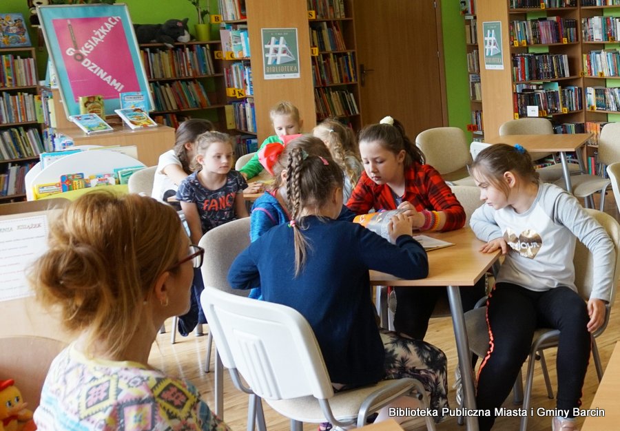 Grupa dzieci siedzi wokół stolika i przegląda zostawioną im książkę.