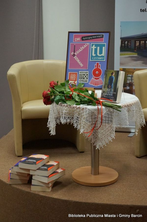 Okrągły stolik stojący na scenie na stoliku stoi wystawka związana z Dkk, leży bukiet róż, pod stolikiem leżą ksiażki