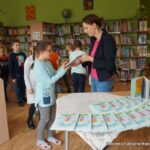 Pani bibliotekarka rozdaje dzieciom książki.