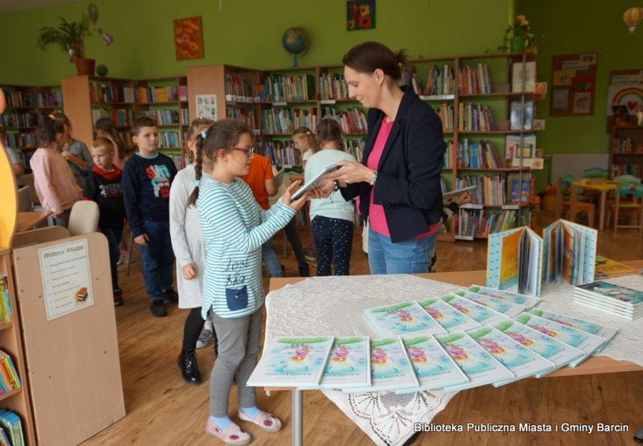 Pani bibliotekarka rozdaje dzieciom książki.