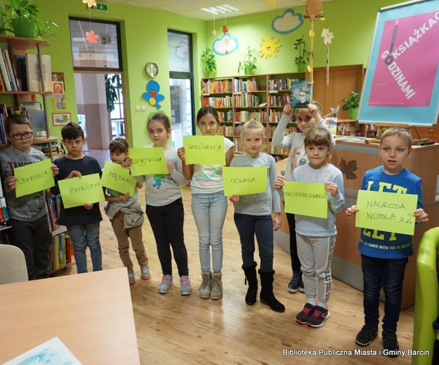 Dzieci stoją w rzędzie i trzymają kratki z napisami opisującymi bohaterkę omawianej książki.
