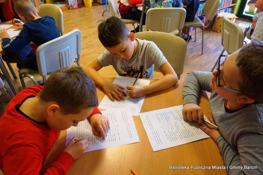 3 chłopców podczas pracy na spotkaniu uzupełnia tekst w brakujących miejscach tekstu wydrukowanego na kartkach papieru.