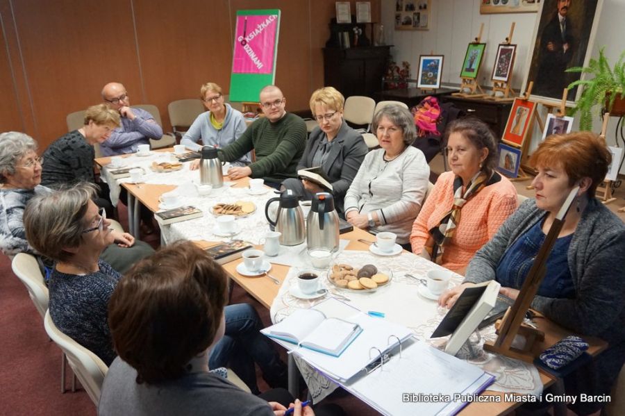 Uczestnicy spotkania siedzący przy stolikach i dyskutujący o omawianej książce.