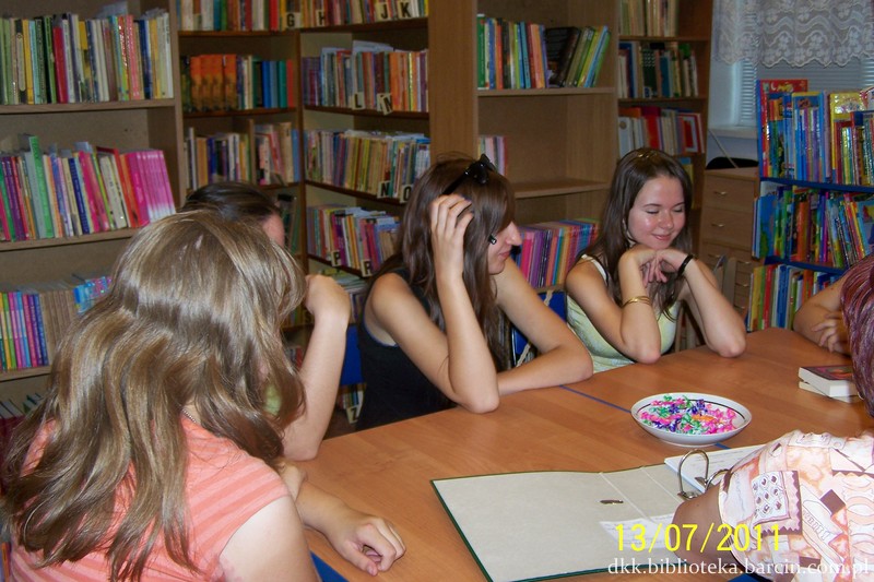 4 uczestniczki siedzące przy stole, na twarzy jednej z nich widać uśmiech, pozostałe są odwrócone od obiektywu aparatu