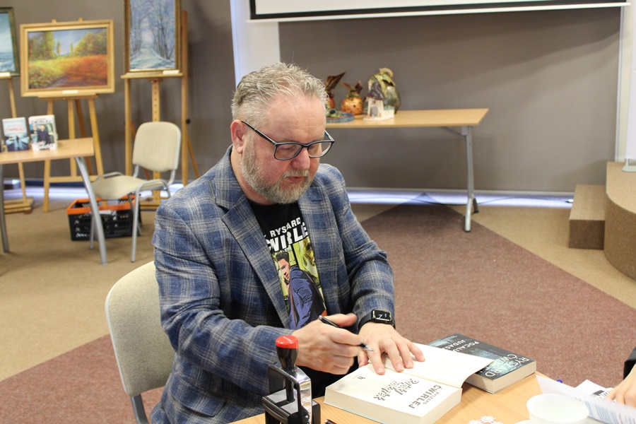 Ryszard Ćwirlej siedzi przy stoliku i podpisuje książkę