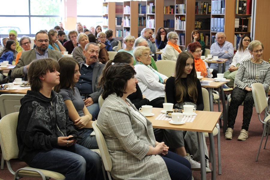 Publiczność podczas spotkania, widać osoby w różnym wieku o różnej płci siedzące na krzesłach i przysłuchujące się rozmowie z młodymi artystami.