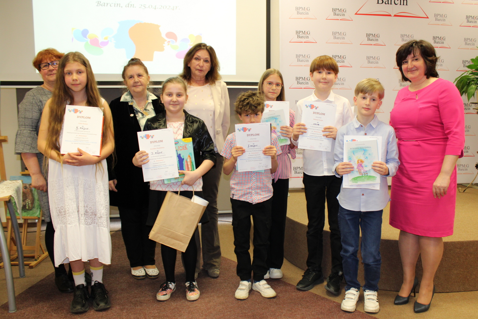 Zdjęcie grupowe pierwszej grupy wiekowej uczestników razem z jury i dyrekcją biblioteki, dzieci trzymają otrzymane nagrody i dyplomy.