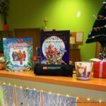 Książki o tematyce Świąt Bożego Narodzenia stojące na ladzie bibliotecznej, wokół książek stoją świąteczne osdoby