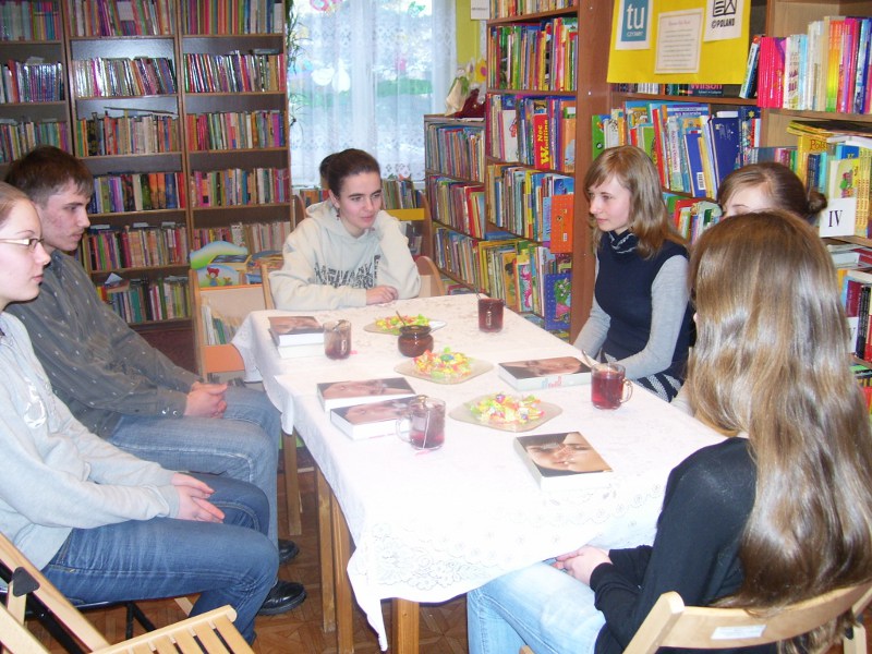 Sześcioro uczestników spotkania siedzących wokół stołu rozmawia o przeczytanej książce.