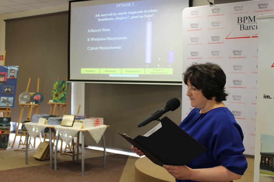 Dyrektor biblioteki czyta jedno z pytań konkursowych, pytanie wyświetlane jest również na ekranie projektora.