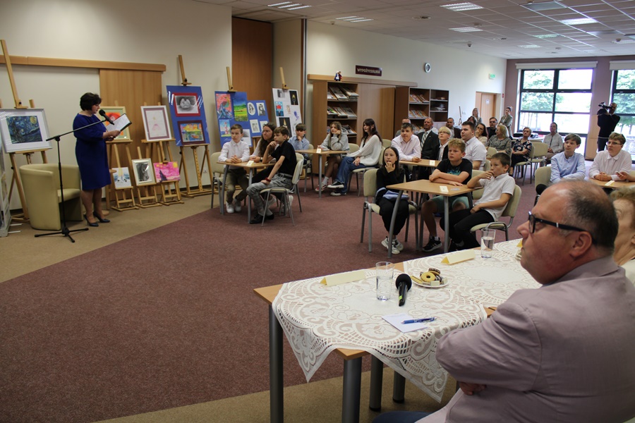 Ludzie zgromadzeni na konkursie, uczestnicy siedzą przy stolikach widownia na krzesłach ustawionych w rzędach