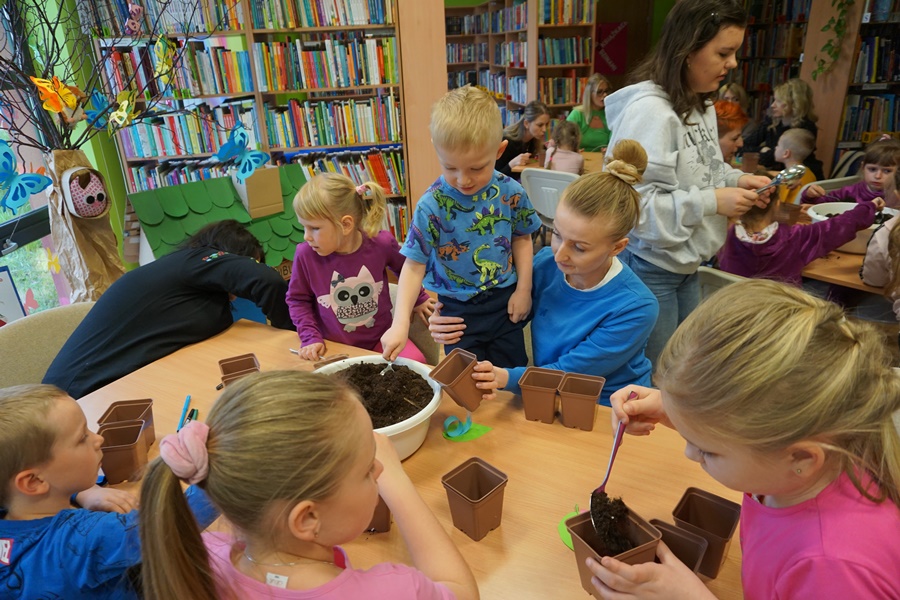 grupa dzieci nabiera ziemię z miski i wsypuje ją do doniczek