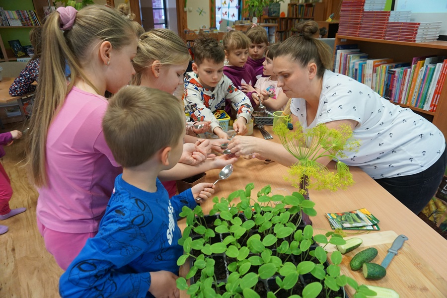 bibliotekarka nakłada dzieciom nasionka na łyżki
