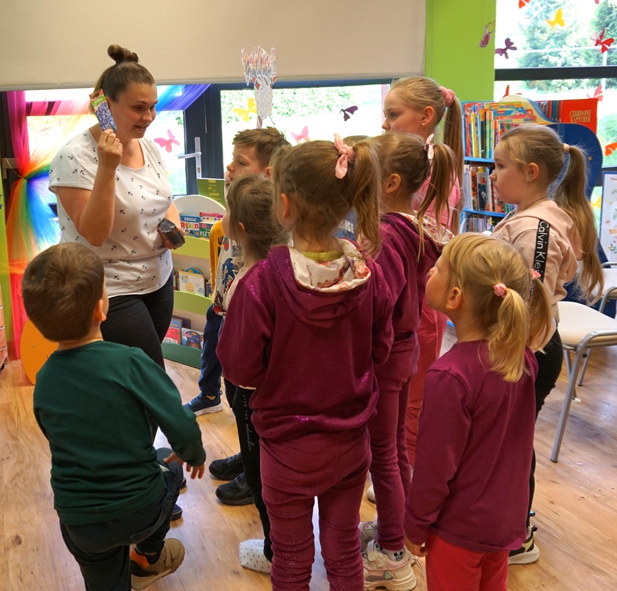 dzieci zebrane przy bibliotekarce, która trzyma paczuszki z nasionami