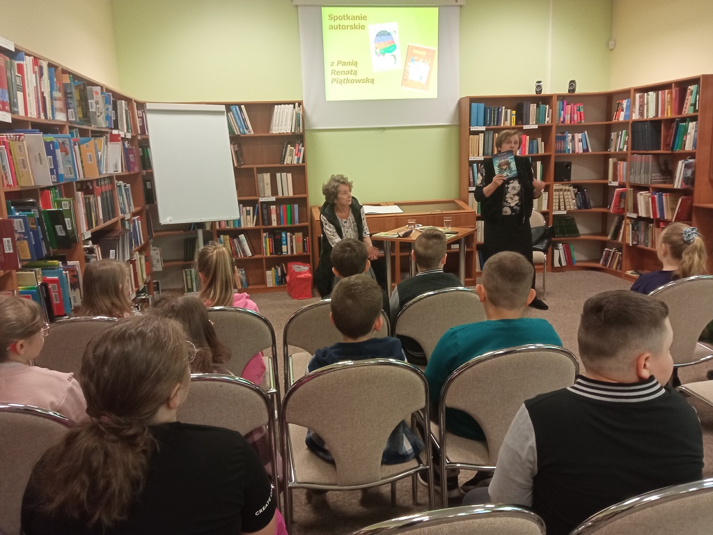 Zaproszone prelegentki stoją przed dziećmi, które siedzą na krzesłach.