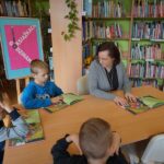 bibliotekarka siedzi przy stole z trzema chłopcami, wszyscy trzymają otwarte ksiażki.