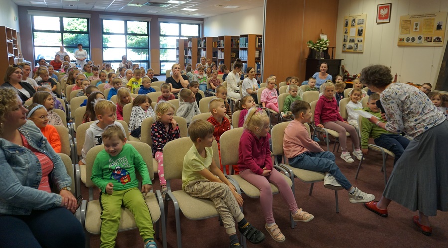 Zaproszona autorka mocno pochylona przechadza się między krzesłami z książką w ręku
