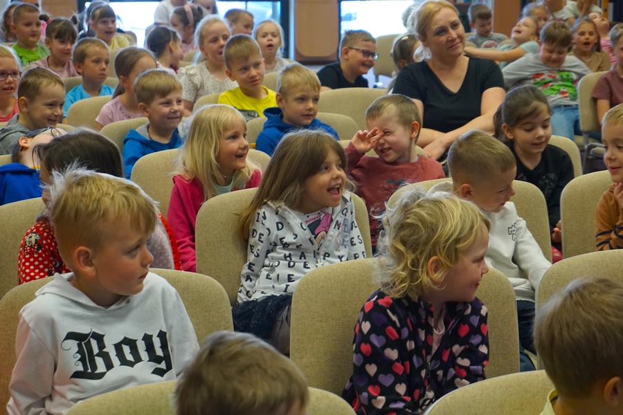 Wycinek widowni zebranej na spotkaniu, dzieci siedzą na krzesłach i szeroko się uśmiechają.
