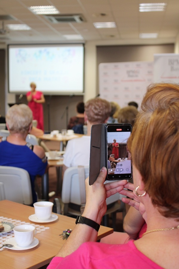 zdjęcie wykonanie pomiędzy publicznością, widać osoby na widowni, jedna z tych osób nagrywa telefonem występ artystki