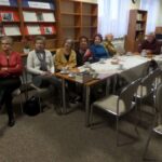 7 osób siedzących na krzesłach patrzy w tę samą stronę