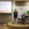 Zespół występujący w trakcie spotkania, kobieta stoi przy mikrofonie na statywie, mężczyzna siedzi na krześle przy instrumencie klawiszowym i mikrofonie na statywie