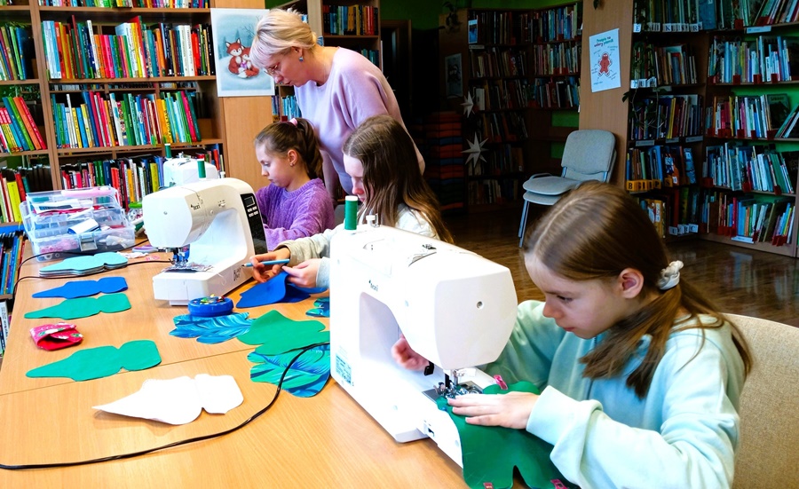 3 uczestniczki zajęć w trakcie korzystania z maszyn do szycia, bibliotekarka nadzoruje pracę grupy
