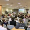 licznie zgromadzona publiczność i uczestnicy konkursu siedzą na krzesłach ustawionych w rzędach i czekają na rozpoczęcie konkursu
