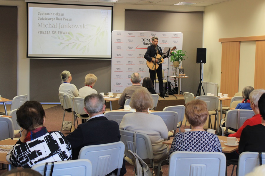 Autor stoi na scenie przed zebraną publicznością i śpiewa swój wiersz grają dodatkowo na gitarze