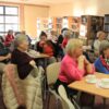 Osoby obecne na spotkaniu siedzą przy stolikach i patrzą w stronesceny