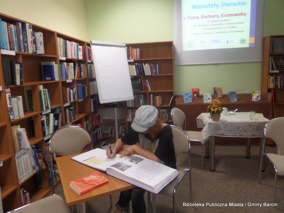 Zaproszona Barbara Kosmowska wpisuje się do księgi pamiątkowej w bibliotece