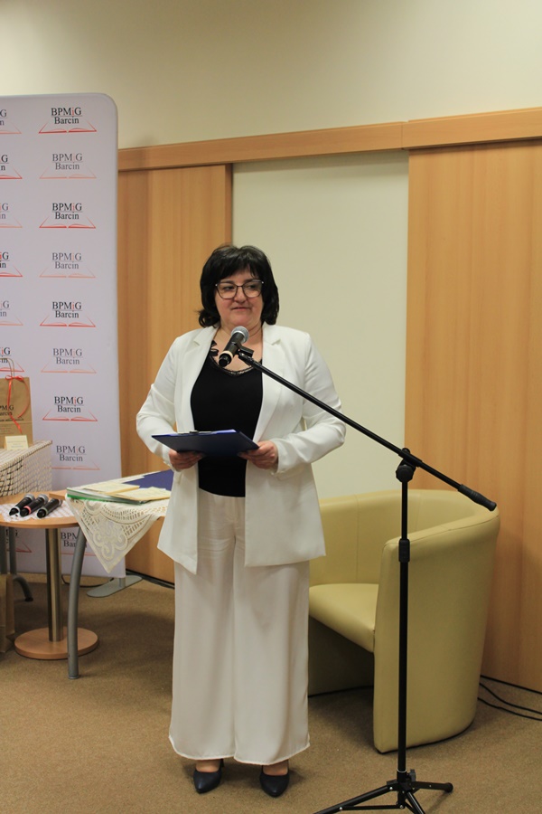 Dyrektorka biblioteki stoi przy mikrofonie i dziękuje uczestnikowi za występ zapraszając kolejną osobę