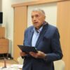 Pan Kaszyński, starszy mężczyzna w granatowym garniturze i niebieskiej koszuli trzyma w rękach otrzymaną w prezencie książkę