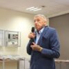 Pan Kaszyński, starszy mężczyzna w granatowym garniturze i niebieskiej koszuli trzyma w ręce mikrofon