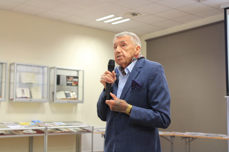 Pan Kaszyński, starszy mężczyzna w granatowym garniturze i niebieskiej koszuli trzyma w ręce mikrofon