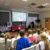 część widowni zebranej na spotkaniu ogląda zdjecia na prezentacji i słucha wypowiedzi