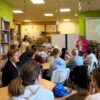 Uczestnicząca w warsztatach młodzież siedzi przy stolikach i słucha bibliotekarek